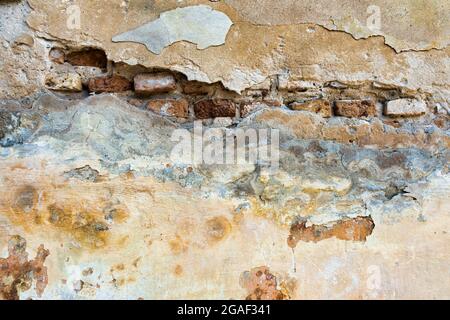 Old cracked weathered plastered brick wall background texture. Dirty peeled plaster wall with falling off flakes of paint Stock Photo