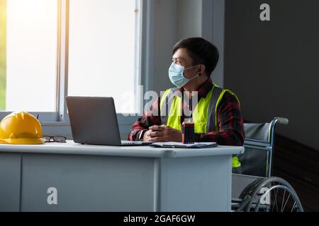 portrait disabled person sitting on wheelchair wear mask working in the office Stock Photo