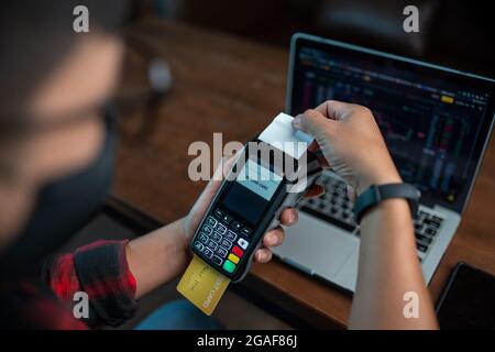 The lifestyle of a young man pays through a credit card machine to buy shares in a coffee shop. Stock Photo