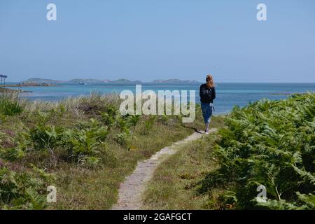 Woman walking on a path through Tresco island, Isles of Scilly, Cornwall, England, UK, July 2021 Stock Photo