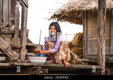 Pretty young Burmese girl washing laundry on deck of wooden stilt house, Inle Lake, Myanmar Stock Photo