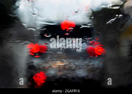 Bokeh, chuva, gotas de água pelo vidro do carro. Dia chuvoso. Lanternas de carros desfocadas. Colorido. Stock Photo