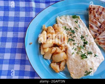 Delicious breakfast of scrambled eggs, potatoes and bread. The food is served on a blue plate. Stock Photo