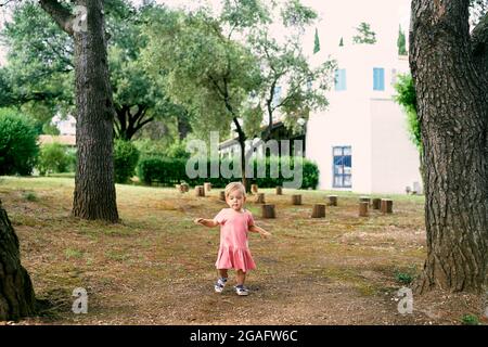 Little girl walks in a clearing near stumps in the courtyard of a house Stock Photo