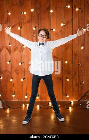 Smart teenager wearing glasses posing in loft apartment. Teenage girl in white shirt on light bulbs background Stock Photo