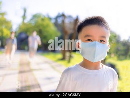 Happy little boy wearing medical mask and walking with parent in the park Stock Photo