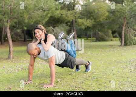 Fitness couple doing push-ups in the park. Woman on back of man Stock Photo