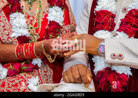 Bride with bridal jewelry and henna decoration on her hand attaches ring to the groom's finger at traditional religious ceremony at a Hindu wedding Stock Photo