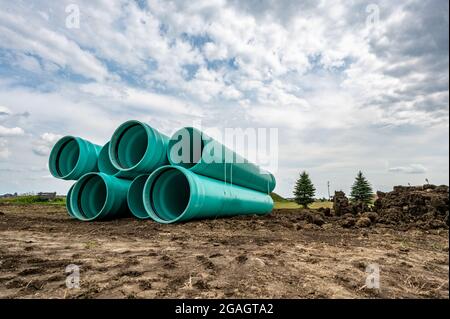 Stacked water main pipe with bell fitting next to an exposed trench for installation Stock Photo