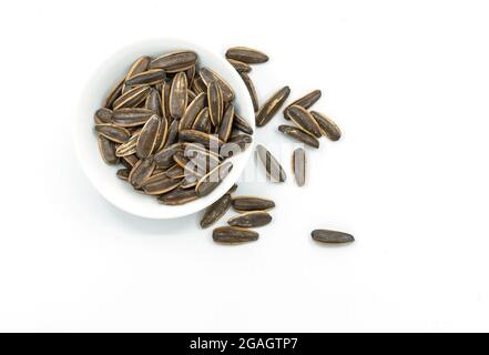 Top view group of roasted sunflower seeds in a white small bowl on white background, some sunflower seeds is spread outside. Stock Photo