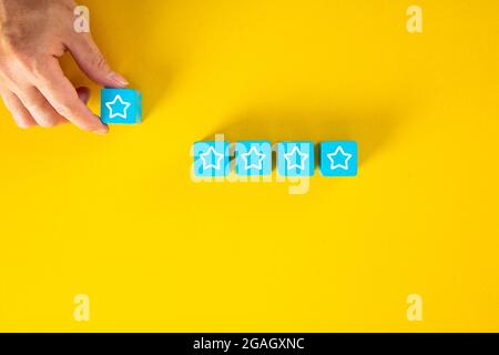 Male hand placing wooden cubes with five star rating on yellow background. Customer experience or satisfaction survey concept. Stock Photo