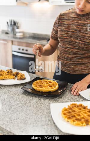 Woman pouring honey and barbecue sauce on waffles next to cereal battered chicken fried steaks Stock Photo