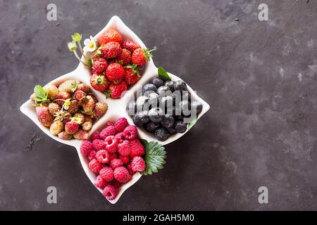 A mixture of fresh berries in a white plate on a dark gray background, natural raw nutrition Stock Photo