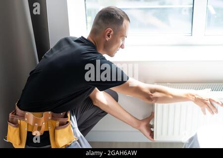 young man plumber checking radiator while installing heating system in apartment Stock Photo