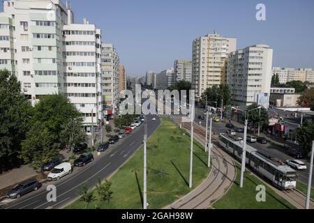 Bucharest, Romania - July 29, 2021: Cars and pedestrians traffic on a busy street of Bucharest with communist era blocks of flats on the sides. Stock Photo