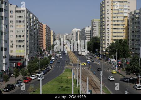 Bucharest, Romania - July 29, 2021: Cars and pedestrians traffic on a busy street of Bucharest with communist era blocks of flats on the sides. Stock Photo