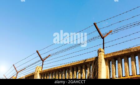Stone wall with barbed wire against blue sky Stock Photo