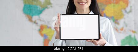 Smiling woman in glasses holds tablet with white blank screen on background of global map of world Stock Photo