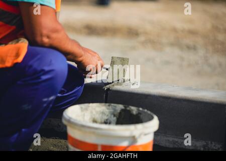 Shallow depth of field (selective focus) image with a worker cementing a sidewalk ledge on a construction site. Stock Photo