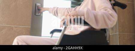 Smiling woman in wheelchair presses button of elevator Stock Photo