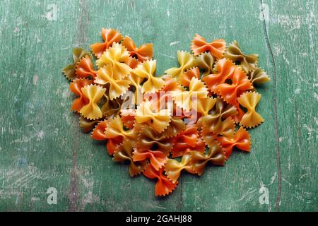 Heart shaped pasta bows on old wooden background