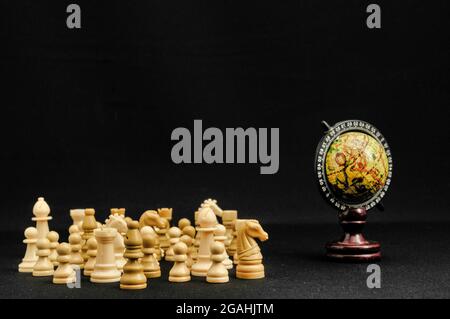 Chess pieces in front of a souvenir globe isolated on a black background Stock Photo