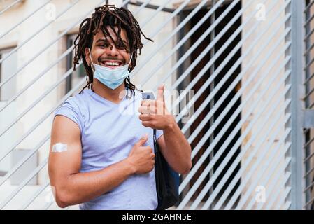 horizontal portrait of a latin american young man. He is proud showing arm after vaccination and doing Ok gesture with fingers Stock Photo