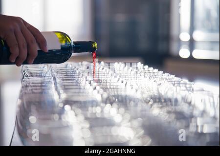 a waiter pouring red wine from bottle to wineglass that set up for dinner reception party in evening time. photo has some flare effect from back light Stock Photo