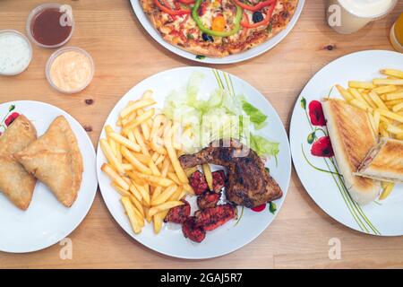 Tandoori chicken with chips and salad, samosas, chicken tikka panini, pizza with dips and drinks Stock Photo