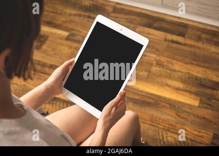 Mockup image with girl in apartment and tablet pc in the hand, wooden background with copy space Stock Photo
