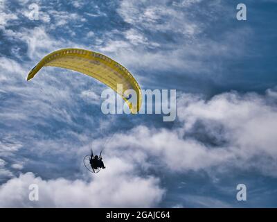 A pilot flies a yellow paramotor above Benone Strand (Beach) on the Atlantic Coast of Northern Ireland. Taken on a sunny day with white clouds. Stock Photo