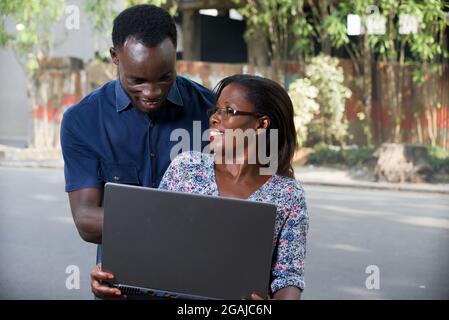 young woman sitting with laptop watching her boyfriend while he looks at the laptop smiling. Stock Photo