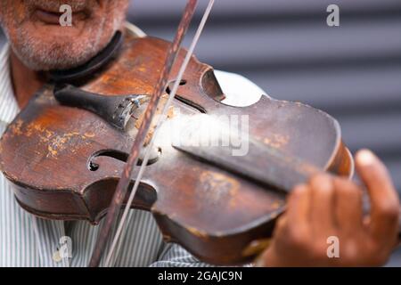 Close up photo of a violin and violin bow which an senior adult man with unshaven wrinkled face playing classical melody being on the street. Stock Photo