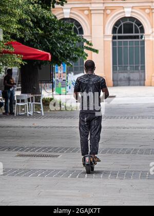 Black Man Dressed in Gray Crossing a Public Square on the Electric Mono Scooter. Stock Photo