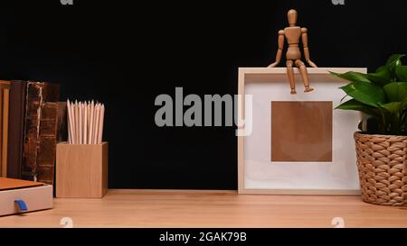 Contemporary workplace with empty frame, pencil holder and old books on wooden table. Stock Photo