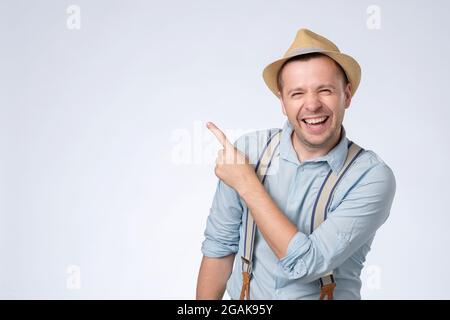 Happy young man in hat pointing aside with forefinger on copyspace. Stock Photo