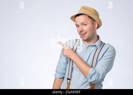 Happy young man in hat pointing aside with forefinger on copyspace. Stock Photo