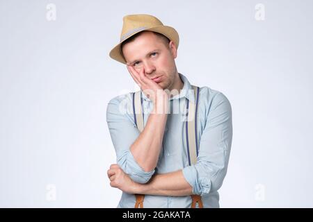 Young man in summer hat with tired, indifferent expression holding hand on cheek Stock Photo