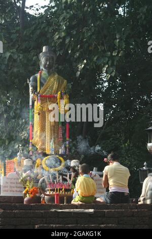 A woman and boy kneeling before a bronze standing Buddha statue, Thailand Stock Photo