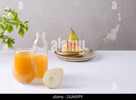 Juice from a pear in a glass and in a bottle, half a pear lies next to it on a white background with copy space Stock Photo