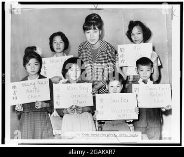 Miss April Lou, teacher at PS 1, Manhattan, with six Chinese children, recent arrivals from Hong Kong and Formosa, who are holding up placards giving his or her Chinese name (both in ideographs and in transliteration) and the name to be entered in official school records, New York, NY, 1964. (Photo by Fred Palumbo/New York World-Telegram & Sun Collection/RBM Vintage Images) Stock Photo