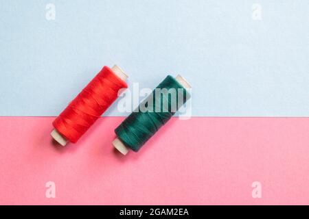 Two sewing thread reels of red and green color on the pink and sky blue colored background. Used selective focus and copy space. Stock Photo