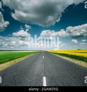 Empty Asphalt Countryside Road Through Fields With Yellow Flowering Canola Rapecolza Canola And Growing Green Wheat Stock Photo