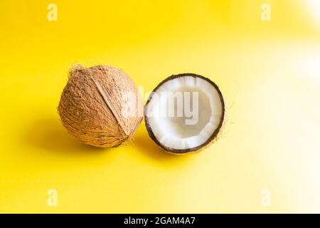 Coconut of which husk removed and one half side of the coconut with shell on the yellow colored background and used selective focus. Stock Photo