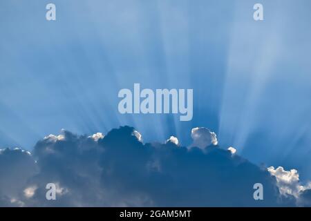 Sun behind the clouds with sun rays streaks in the cloudy blue sky with copy space. Stock Photo