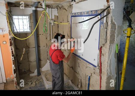 Builder removing a mirror from a wall with a hammer. House renovation. Stock Photo