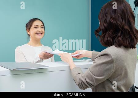 receptionist accepts documents from the female visitor Stock Photo