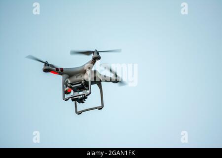 A drone flying in an open sky, capturing aerial footage during daylight Stock Photo