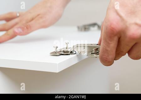 the carpenter screws the hinge on the furniture door. Furniture assembly service concept Stock Photo