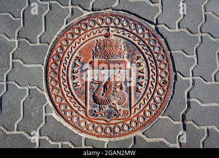 Manhole cover in Kazan, Tatarstan, Russia. Sewer lid with coat of arms of Kazan on road. Top view of metal manhole cap on city street. Traditional dra Stock Photo